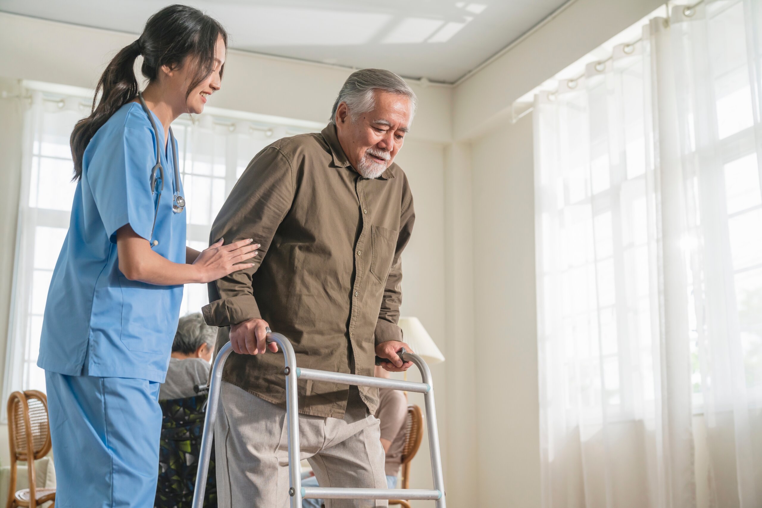 A young nurse holds the arm of a elderly man using a walker