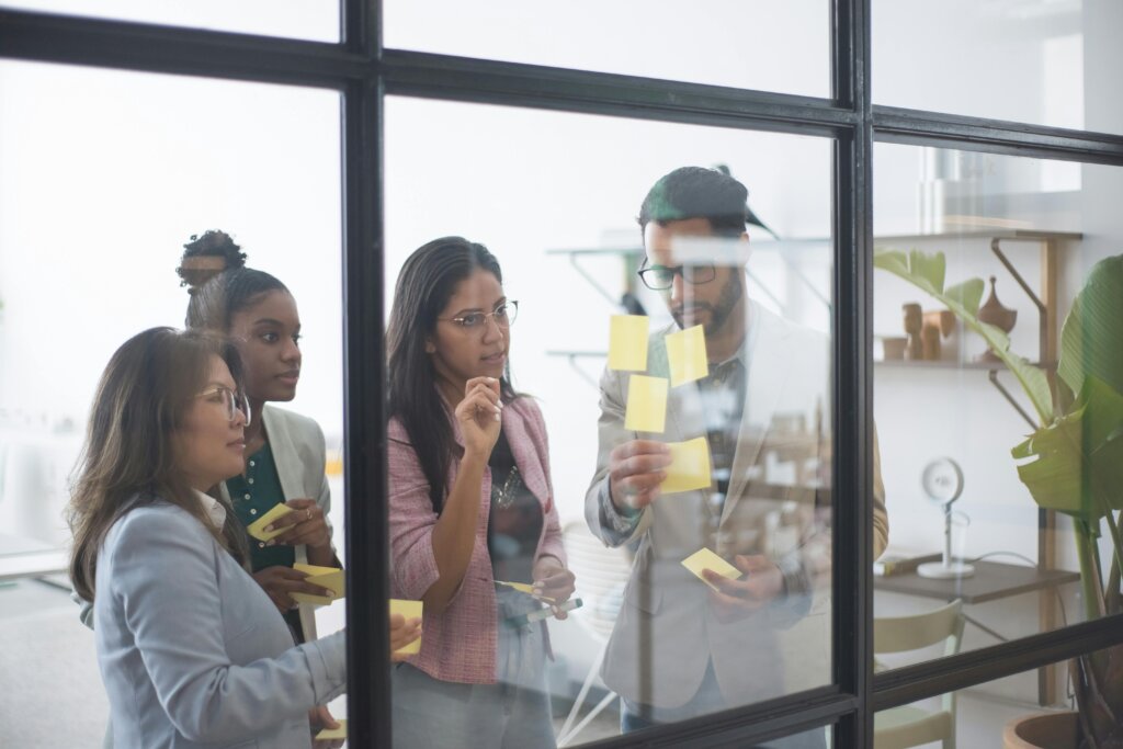 a diverse group of young people placing sticky notes on a glass wall